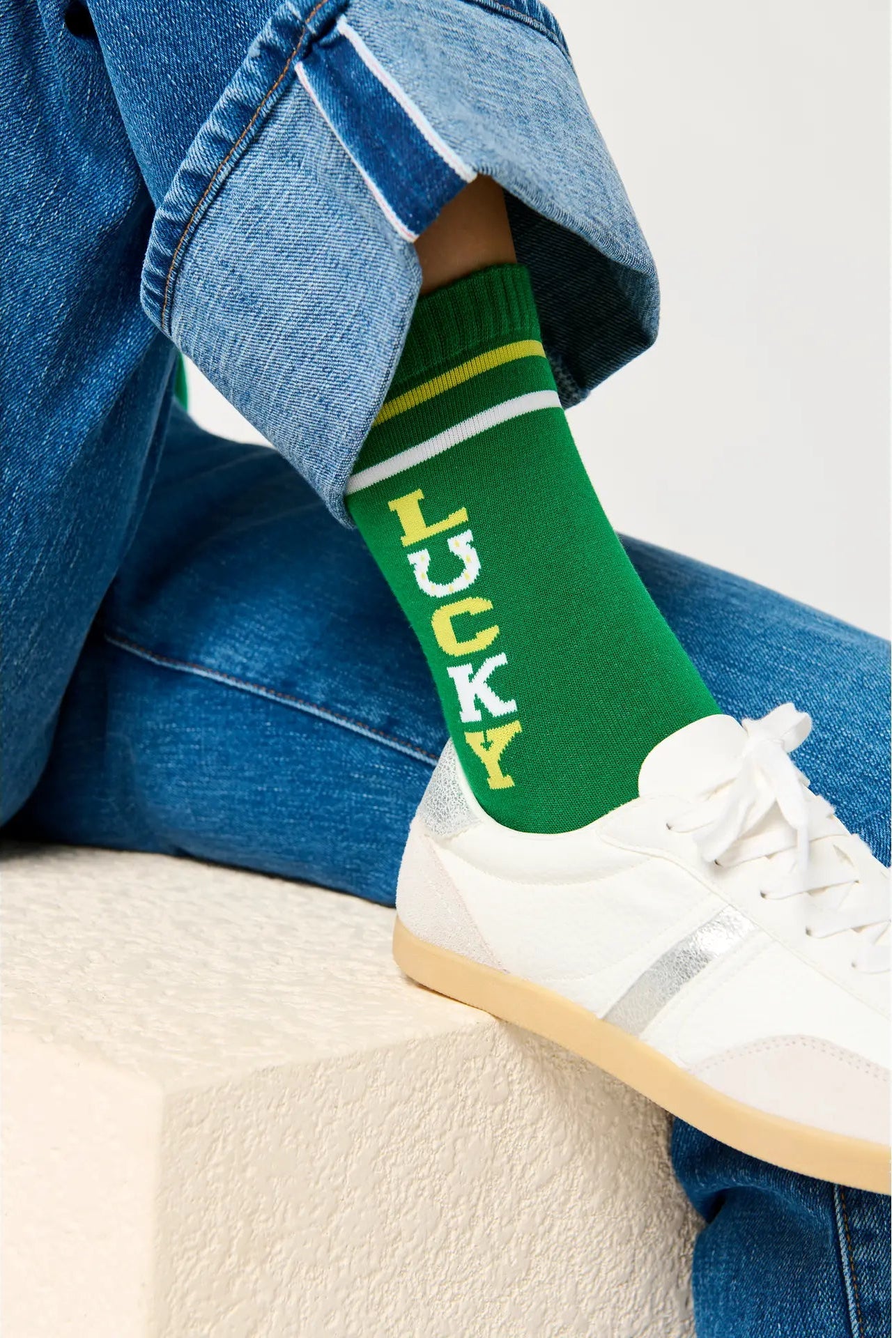 Green sock with 'LUCKY' text worn by a person sitting on a white surface.
