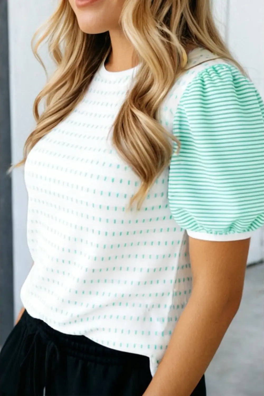 Woman wearing a white and green striped shirt with black pants.