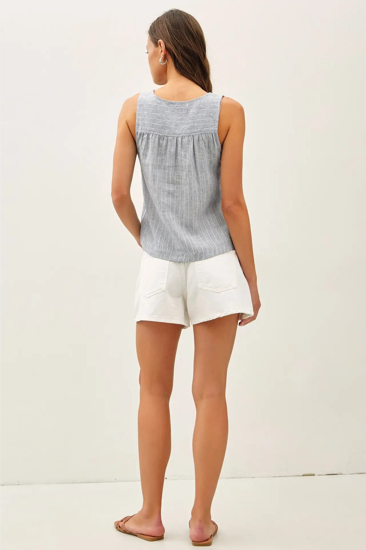 Woman wearing a sleeveless blue and white checkered top and white shorts on a plain background