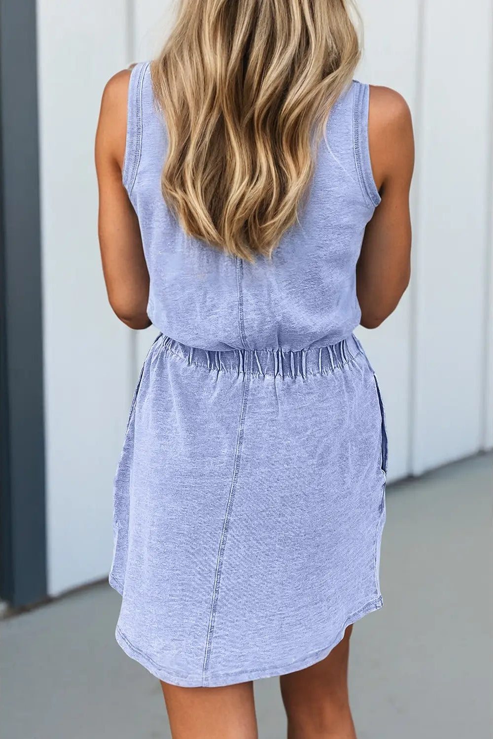 Woman wearing a light blue sleeveless dress against a white wall.