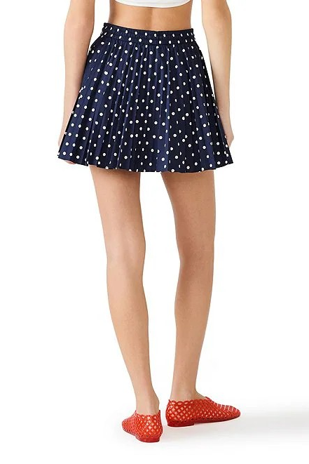 Person wearing a navy blue polka dot skirt with red shoes on a white background