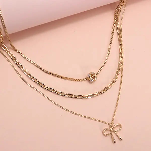 Gold chain necklaces with bow and round charm on a pink background
