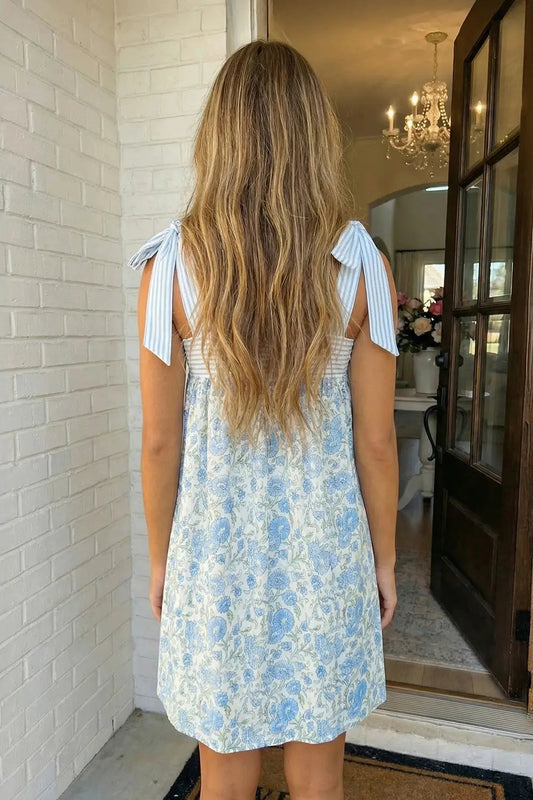 Woman wearing a light blue floral dress with tie shoulders in a home setting.