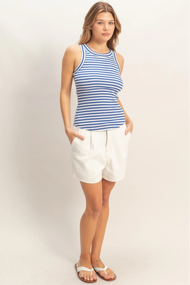 Woman wearing a blue and white striped tank top and white shorts on a light background