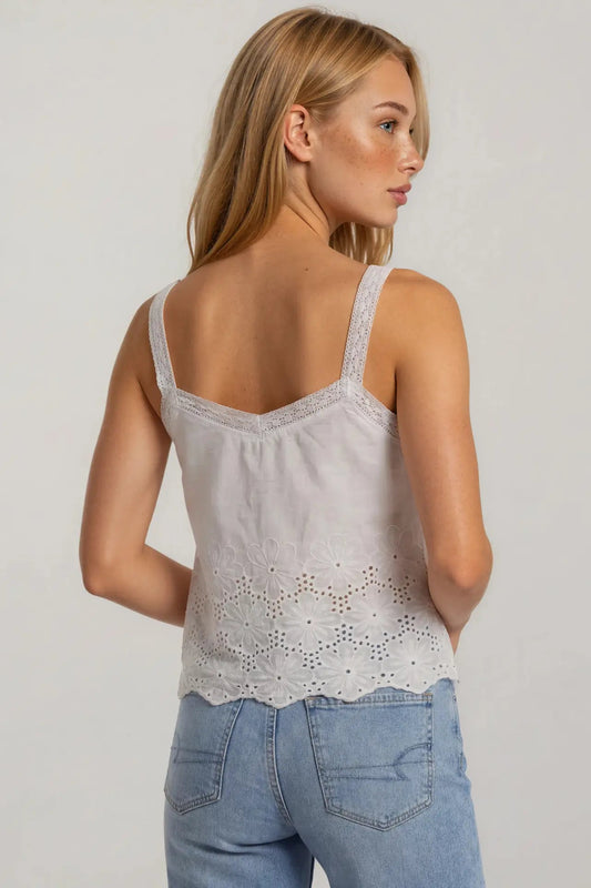 Woman wearing a light gray lace tank top and blue jeans on a plain background