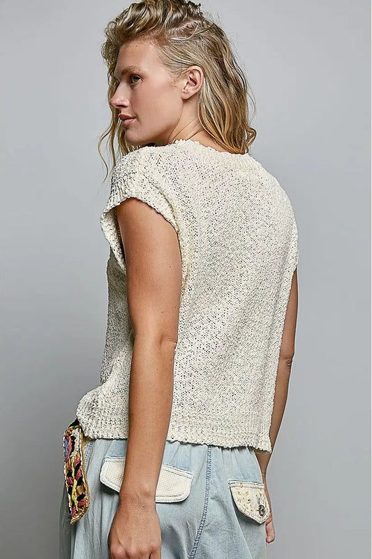 Woman wearing a textured beige top and light blue jeans against a gray background