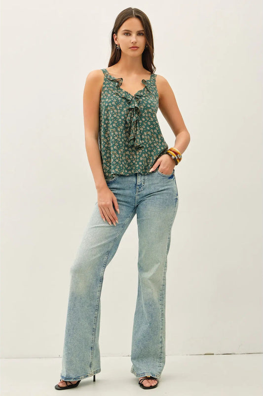 Woman wearing a green patterned top and light blue jeans on a white background