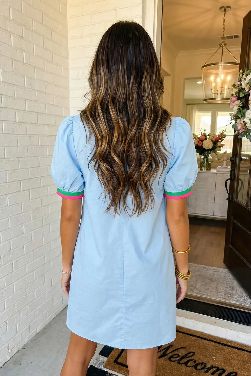 Woman wearing a light blue dress with colorful trim in a home setting.