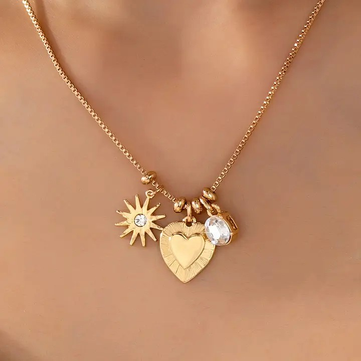 Gold necklace with heart, sun, and round charm on a blurred background
