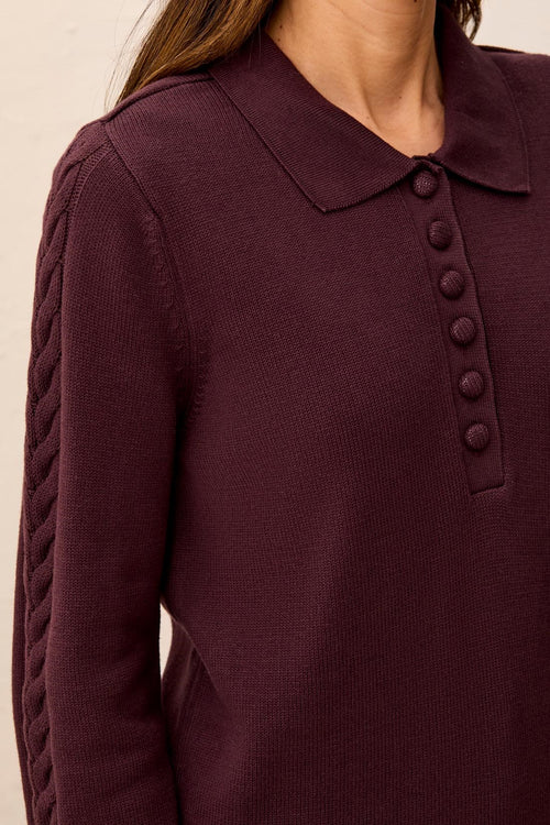 Close-up of a maroon sweater with a collar and button details on a neutral background