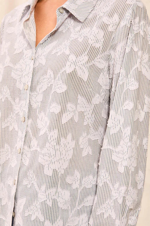 Close-up of a button-front collared shirt with a fine vertical stripe pattern in light gray and white, overlaid with a white floral lace or embroidered pattern.