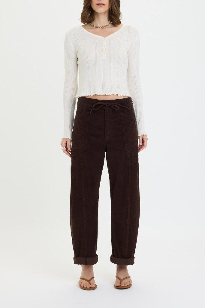 Person wearing a white long-sleeve top and brown pants on a white background