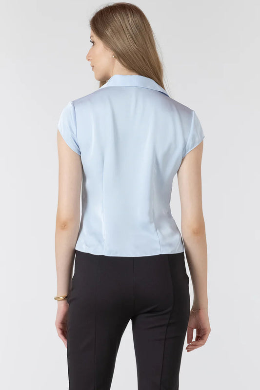 Woman wearing a light blue sleeveless blouse and black pants on a white background