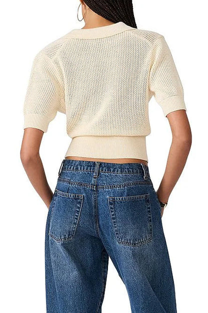 A woman shown from the back wearing a cream-colored short-sleeve knit cropped top and blue jeans against a plain white background.