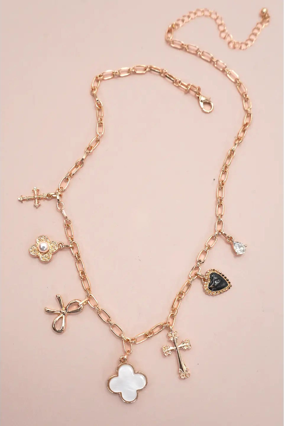 Rose gold necklace with various charms on a pink background