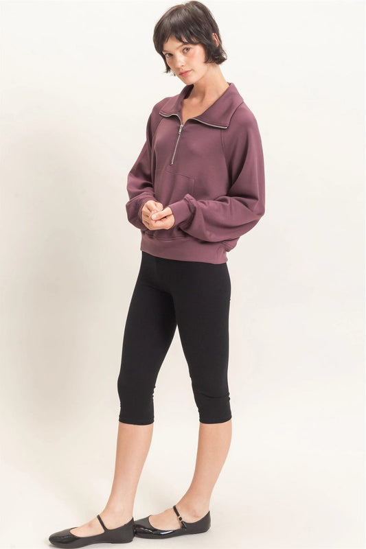 Woman wearing a purple zip-up sweatshirt and black leggings on a white background