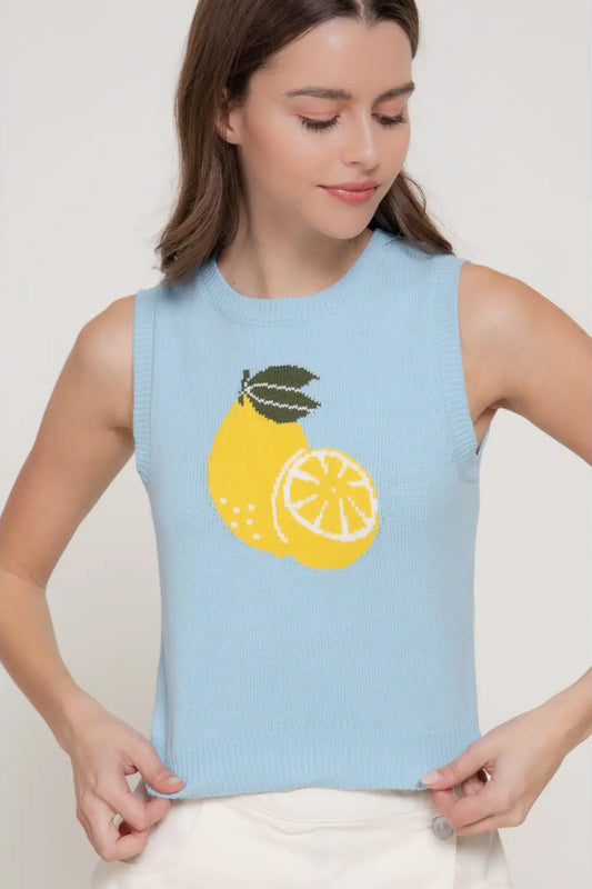 Woman wearing a light blue sleeveless sweater with lemon design on a plain background