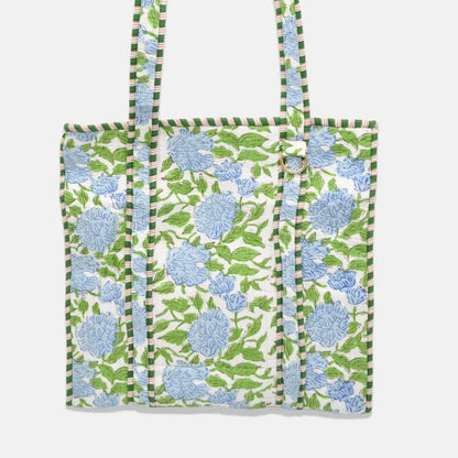 A fabric tote bag featuring a green and blue floral block-print pattern on a white background, with striped green and white handles, shown against a light gray background.