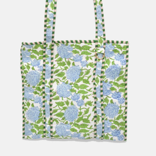 A fabric tote bag featuring a green and blue floral block-print pattern on a white background, with striped green and white handles, shown against a light gray background.