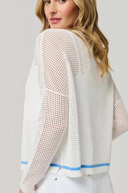 Woman wearing a white knit cardigan with blue trim on a light gray background