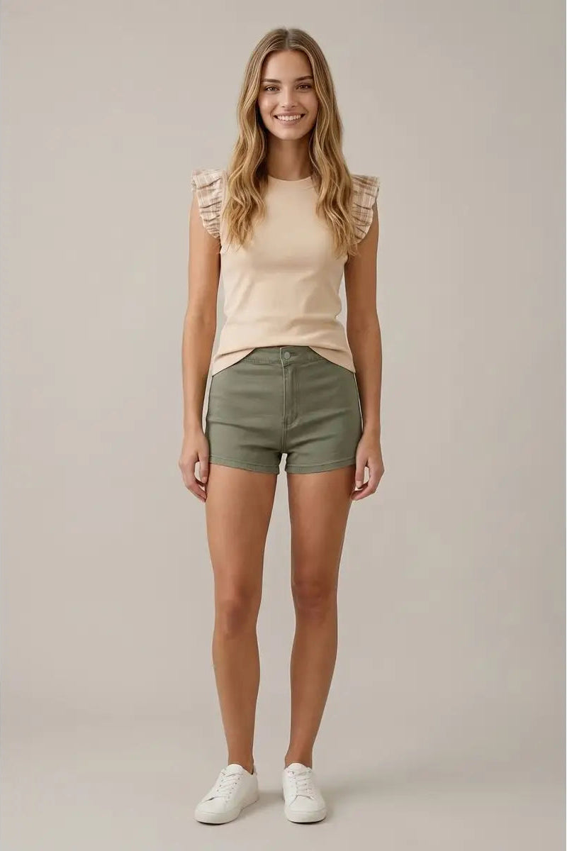 Woman wearing a beige top and green shorts against a plain background