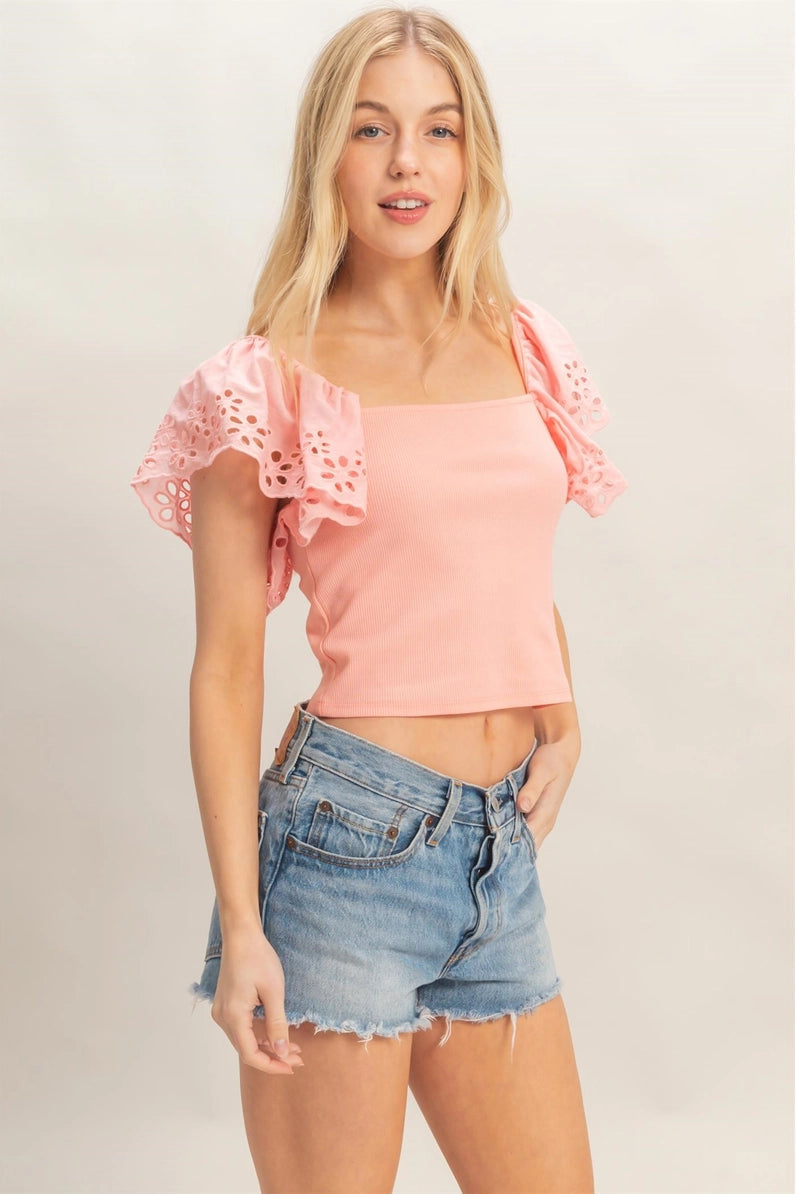 Woman wearing a pink top with lace sleeves and denim shorts on a plain background