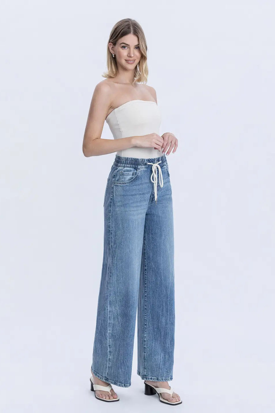 Woman wearing a strapless top and wide-leg jeans on a white background