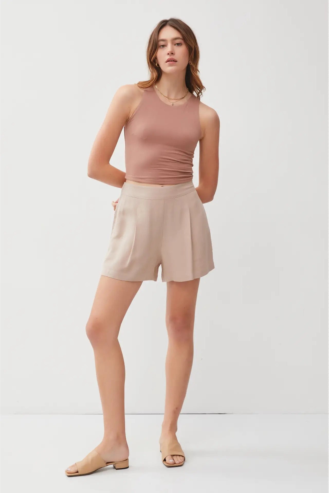 Woman wearing a pink sleeveless top and beige shorts on a white background