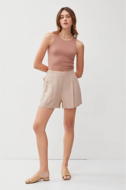 Woman wearing a pink sleeveless top and beige shorts on a white background