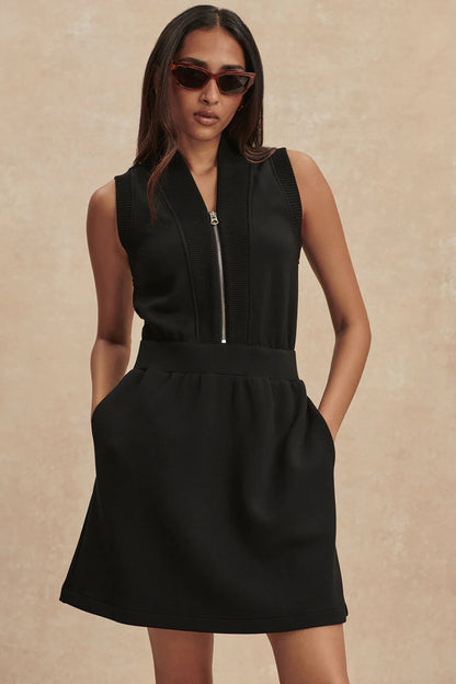 Woman wearing a black sleeveless dress with a zipper on a beige background