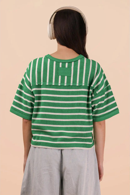 Person wearing a green and white striped shirt with a logo on a beige background