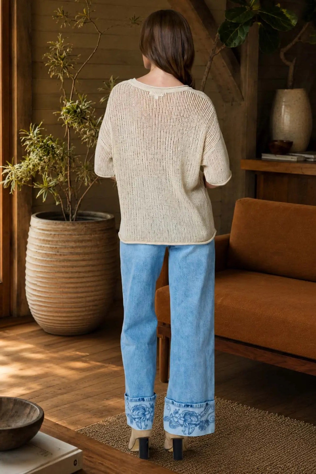 Person wearing a beige sweater and blue jeans standing in a cozy living room.