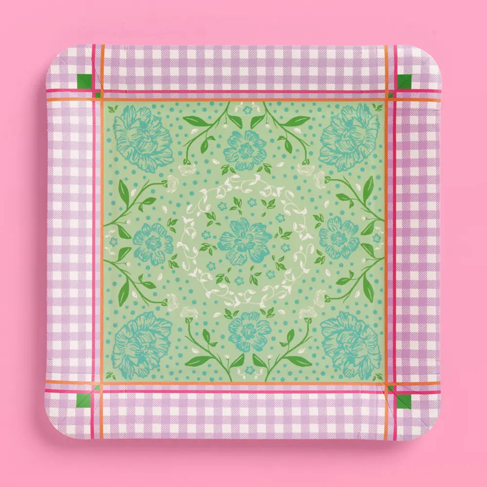 A square paper plate with rounded corners, featuring a light green central floral pattern surrounded by a pink and white gingham border, set against a solid pink background.