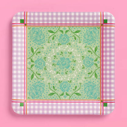 A square paper plate with rounded corners, featuring a light green central floral pattern surrounded by a pink and white gingham border, set against a solid pink background.