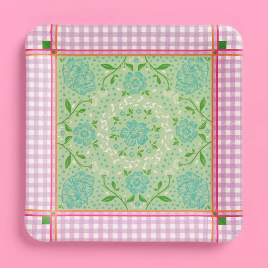 A square paper plate with rounded corners, featuring a light green central floral pattern surrounded by a pink and white gingham border, set against a solid pink background.