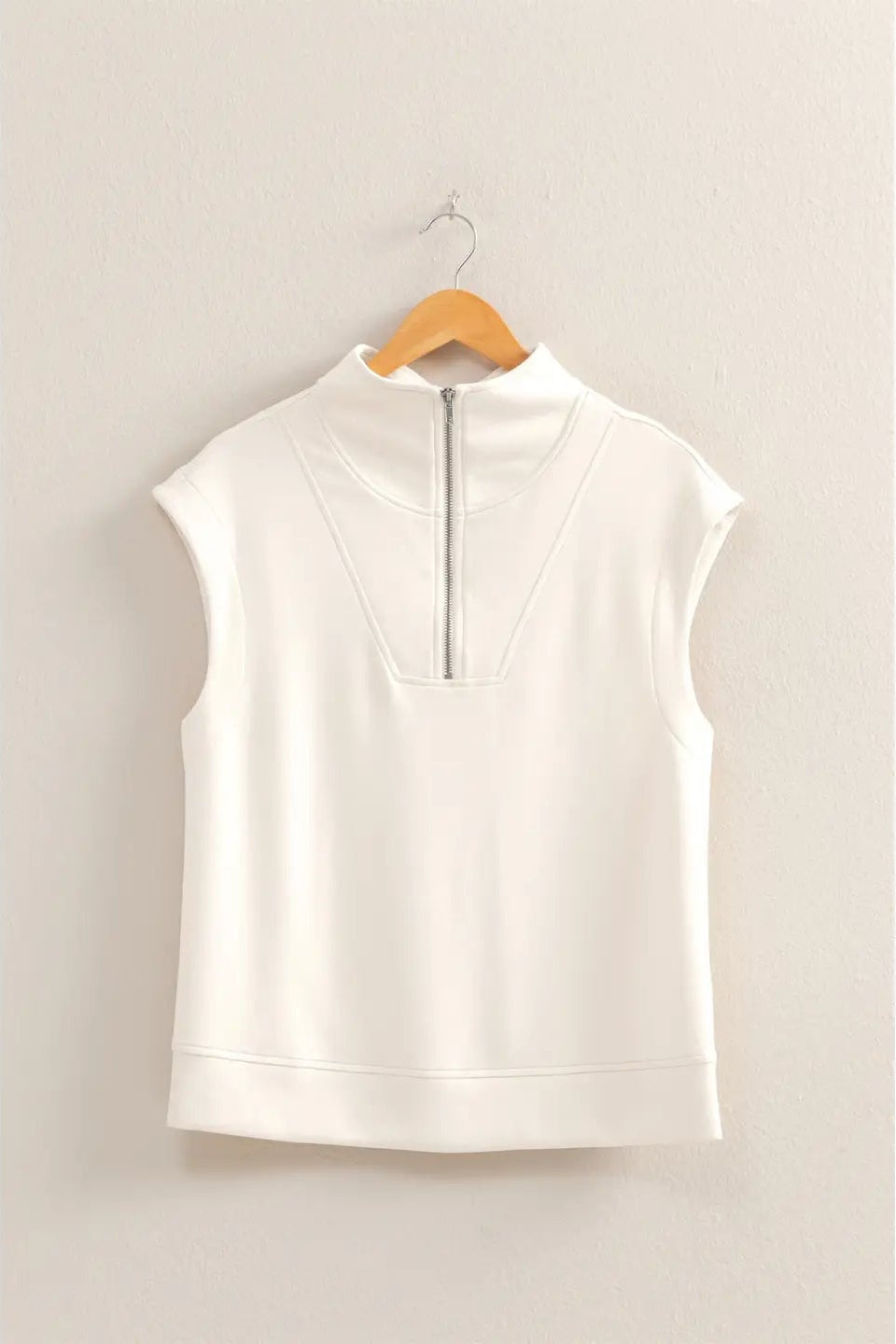 White sleeveless top on a wooden hanger against a beige wall