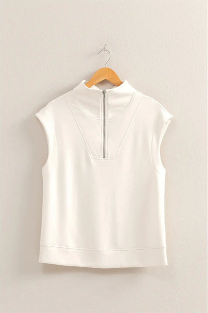 White sleeveless top on a wooden hanger against a beige wall
