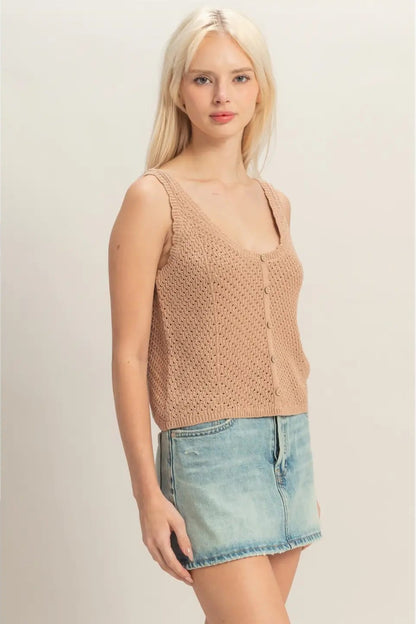 Woman wearing a beige knitted tank top and denim shorts on a plain background