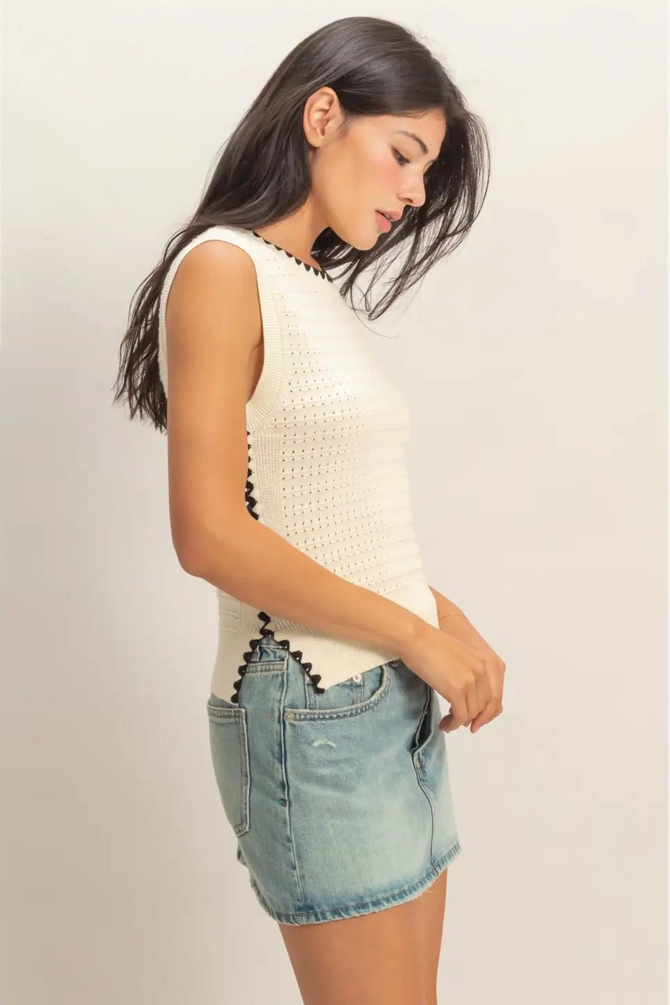 Woman wearing a white sleeveless top and denim shorts on a plain background