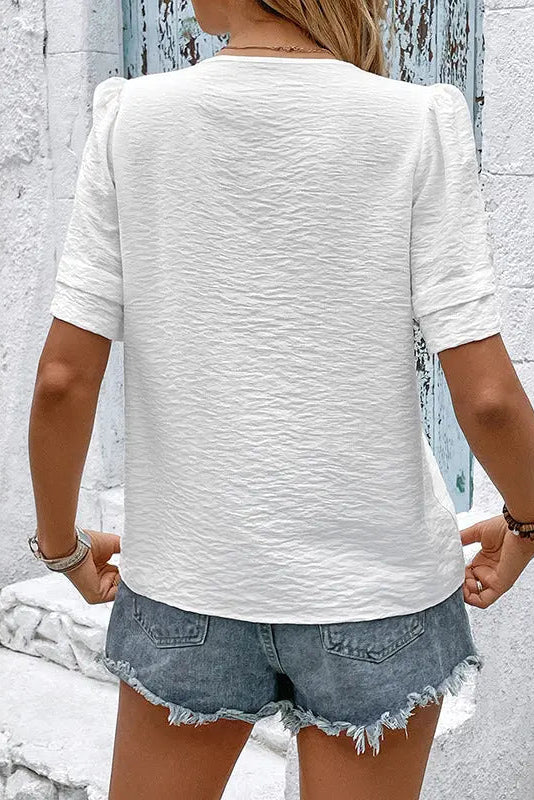 Person wearing a white textured shirt and denim shorts against a light gray wall.
