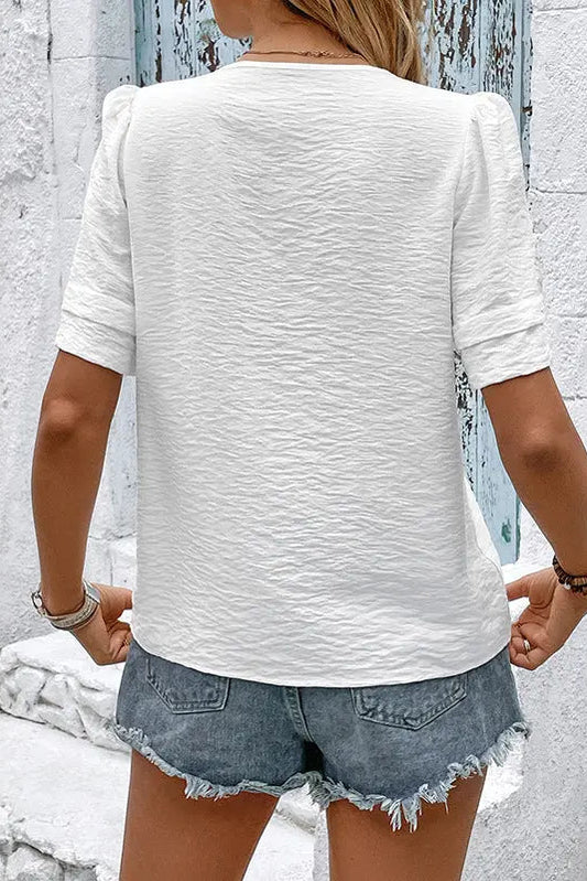 Person wearing a white textured shirt and denim shorts against a light gray wall.