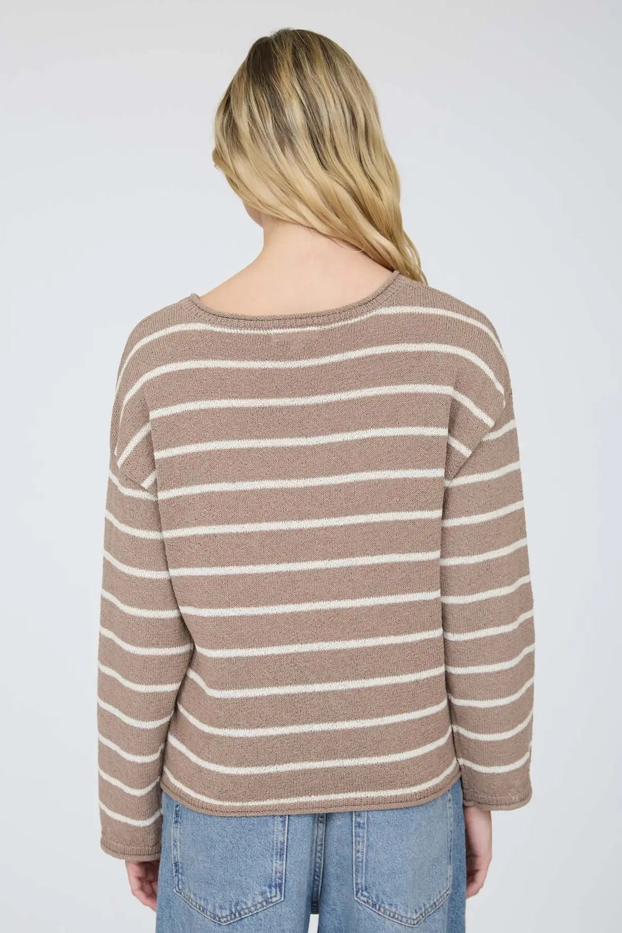 Person wearing a striped sweater and jeans on a plain background