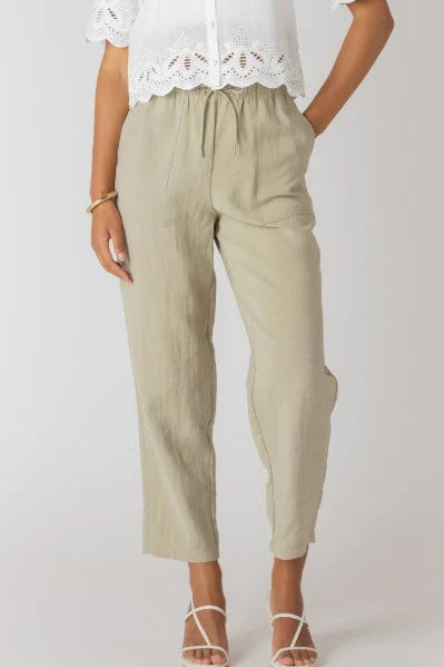 Person wearing beige pants and a white lace top on a plain background