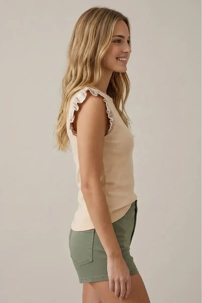Woman wearing a beige sleeveless top and green shorts against a plain background