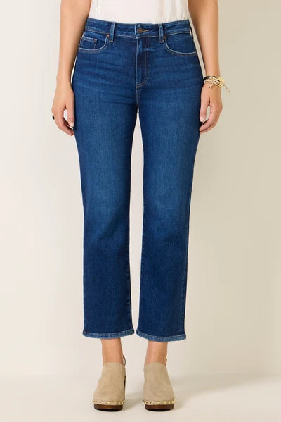 A model wearing a pair of dark blue cropped jeans with a straight-leg fit, paired with beige ankle boots and a white top, standing against a plain beige background.