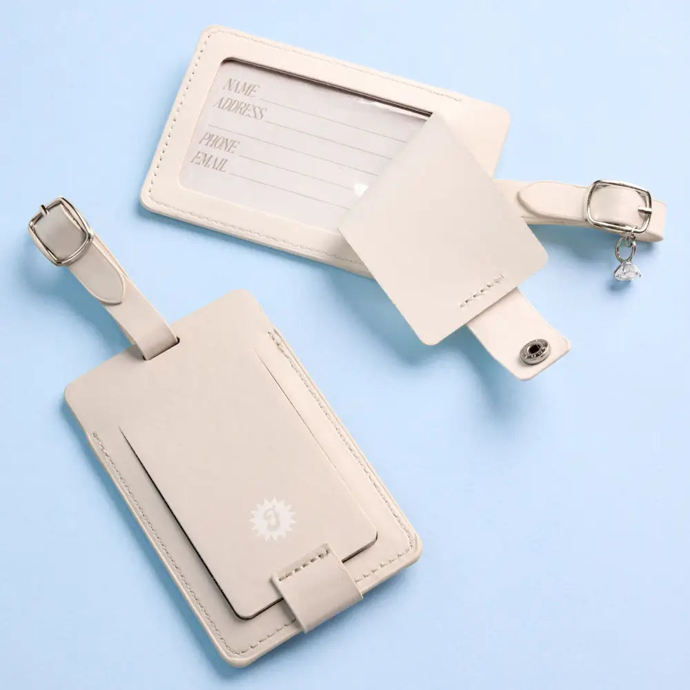 Two beige luggage tags with a buckle on a light blue background