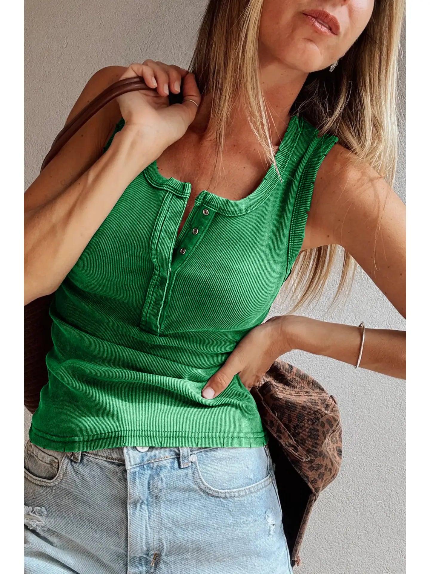 Woman wearing a green tank top and light blue jeans, holding a leopard print jacket.
