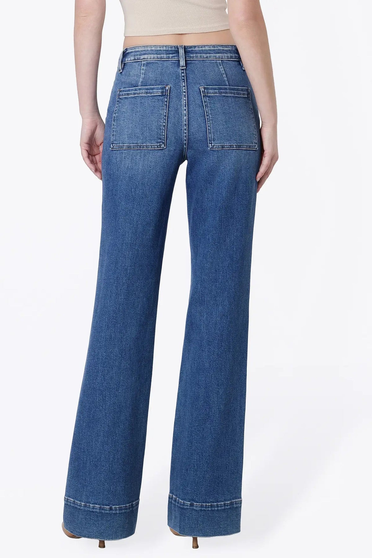 Rear view of a model wearing blue wide-leg jeans with a cuffed hem and back pocket details, paired with a beige crop top against a white studio background.