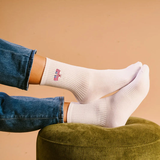White socks with a small flag design worn by a person sitting on a green cushion against a beige background