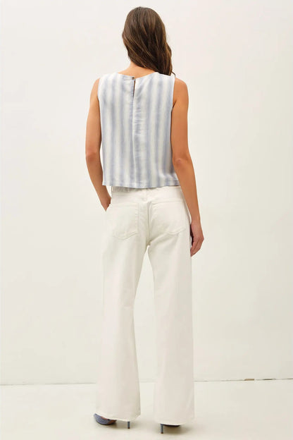 Woman wearing a sleeveless striped top and white pants on a plain background